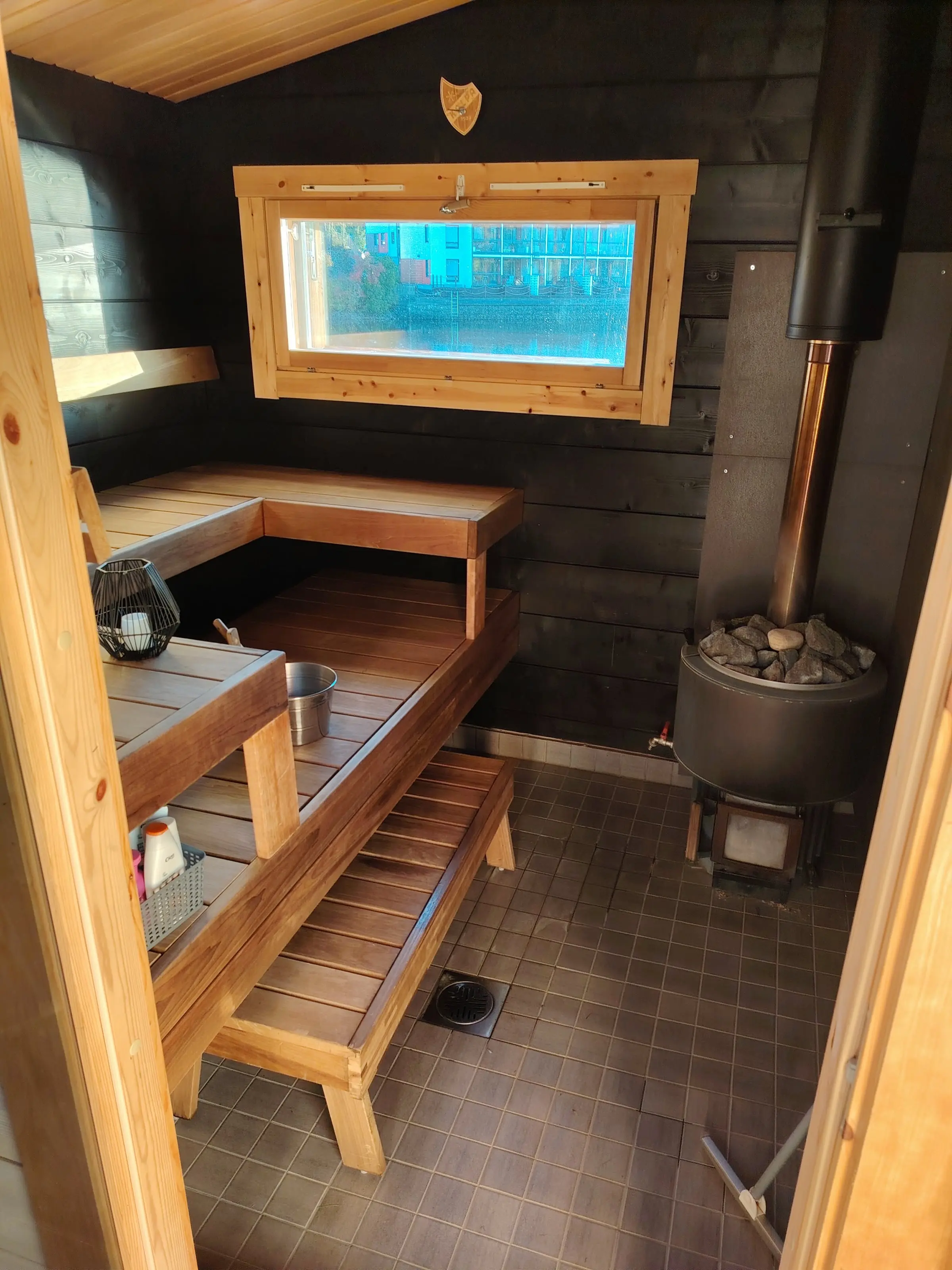 The sauna room from the doorway: two tiers of benches, a window and the wood-burning stove.