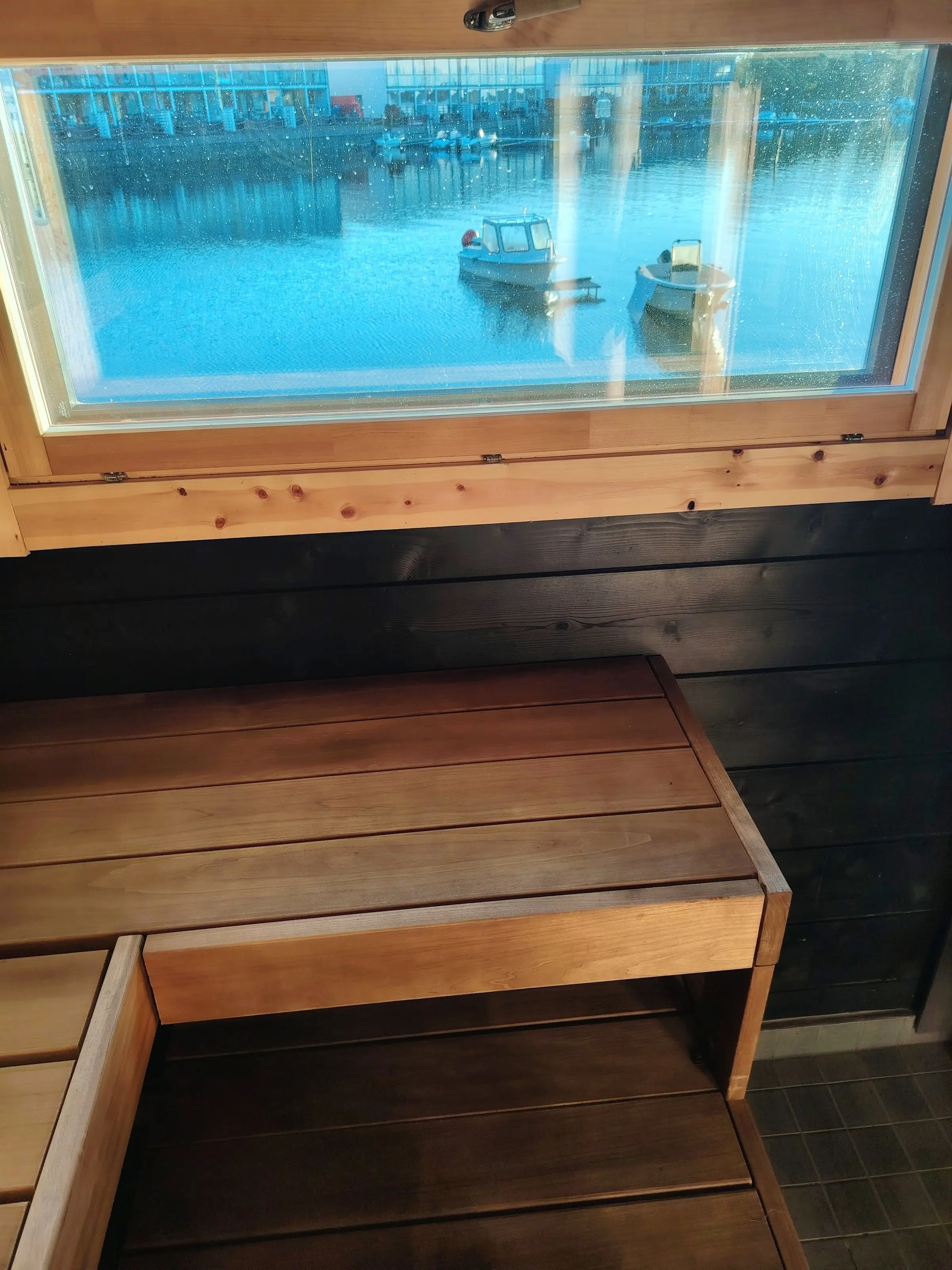 View from the sauna bench through the window to boats on the lake and buildings on the far shore.
