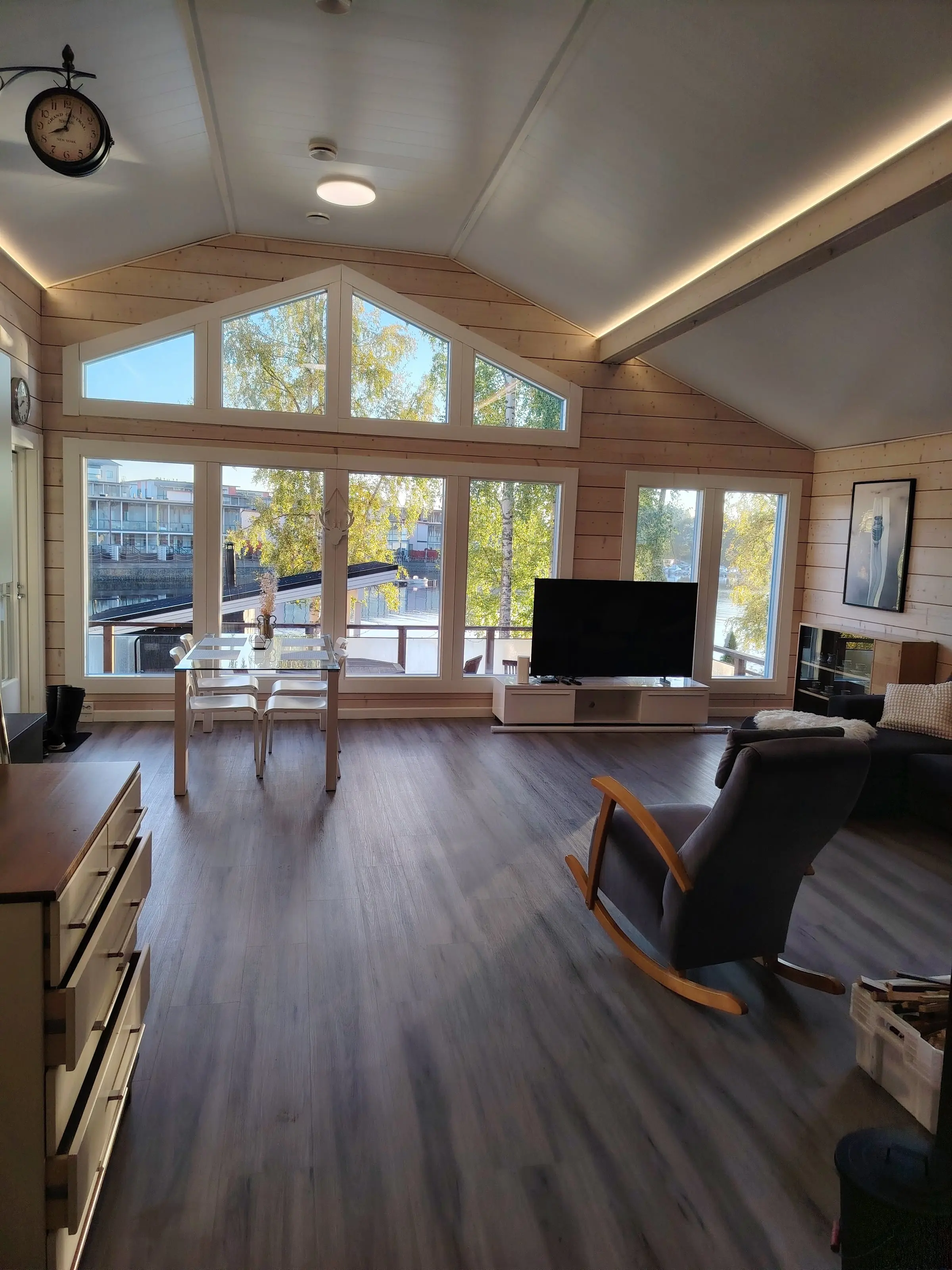 The open living room under a high vaulted ceiling, with a dining table by the tall windows.