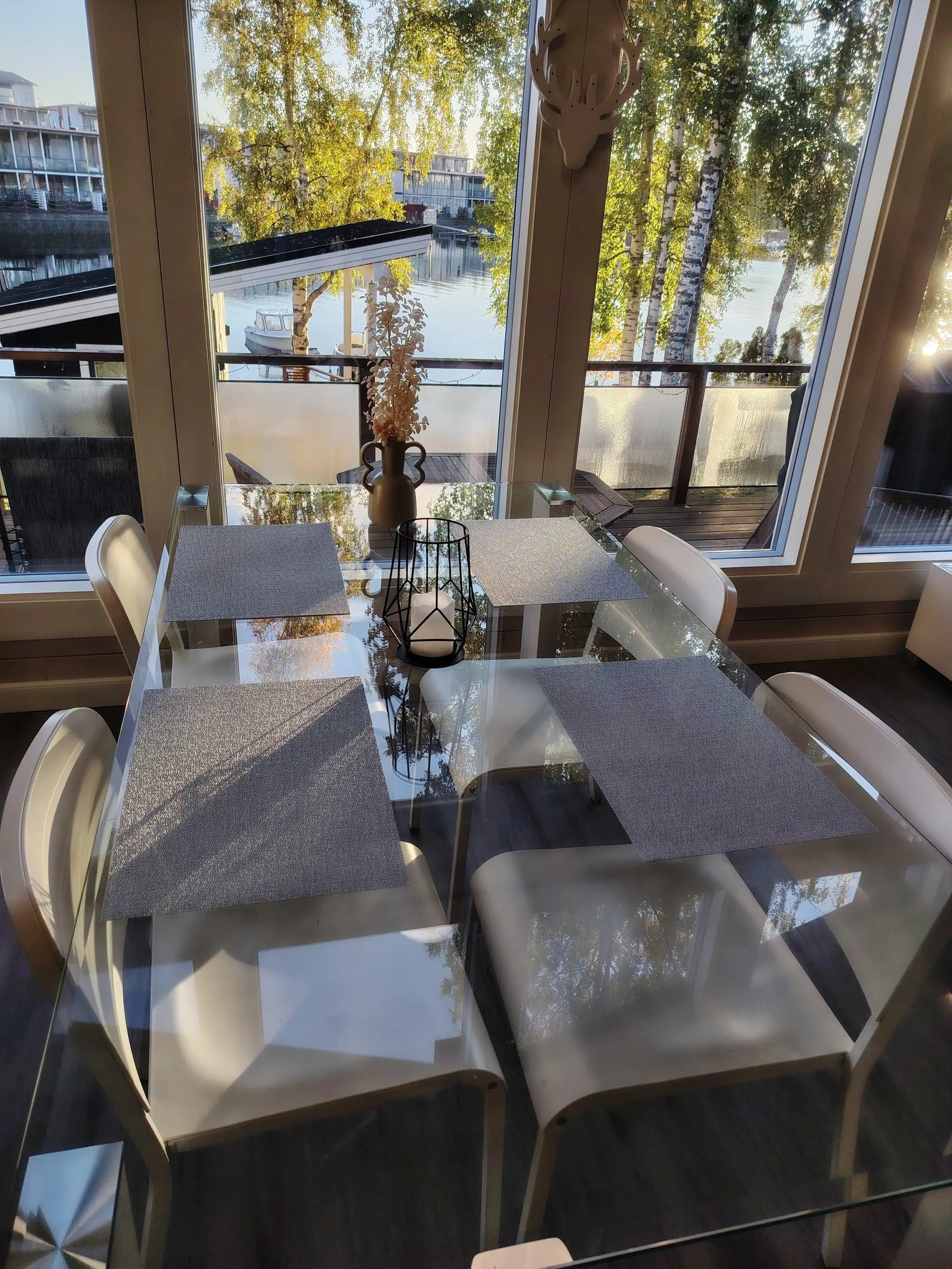 The dining table by the windows, looking out over the terrace to Rantasauna's roof, birches and the lake.